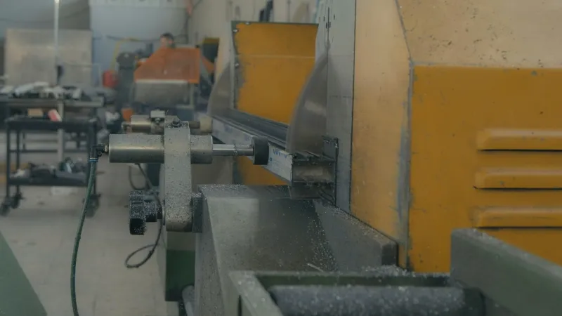 Industrial saw cutting a steel section, with metal shavings in the air