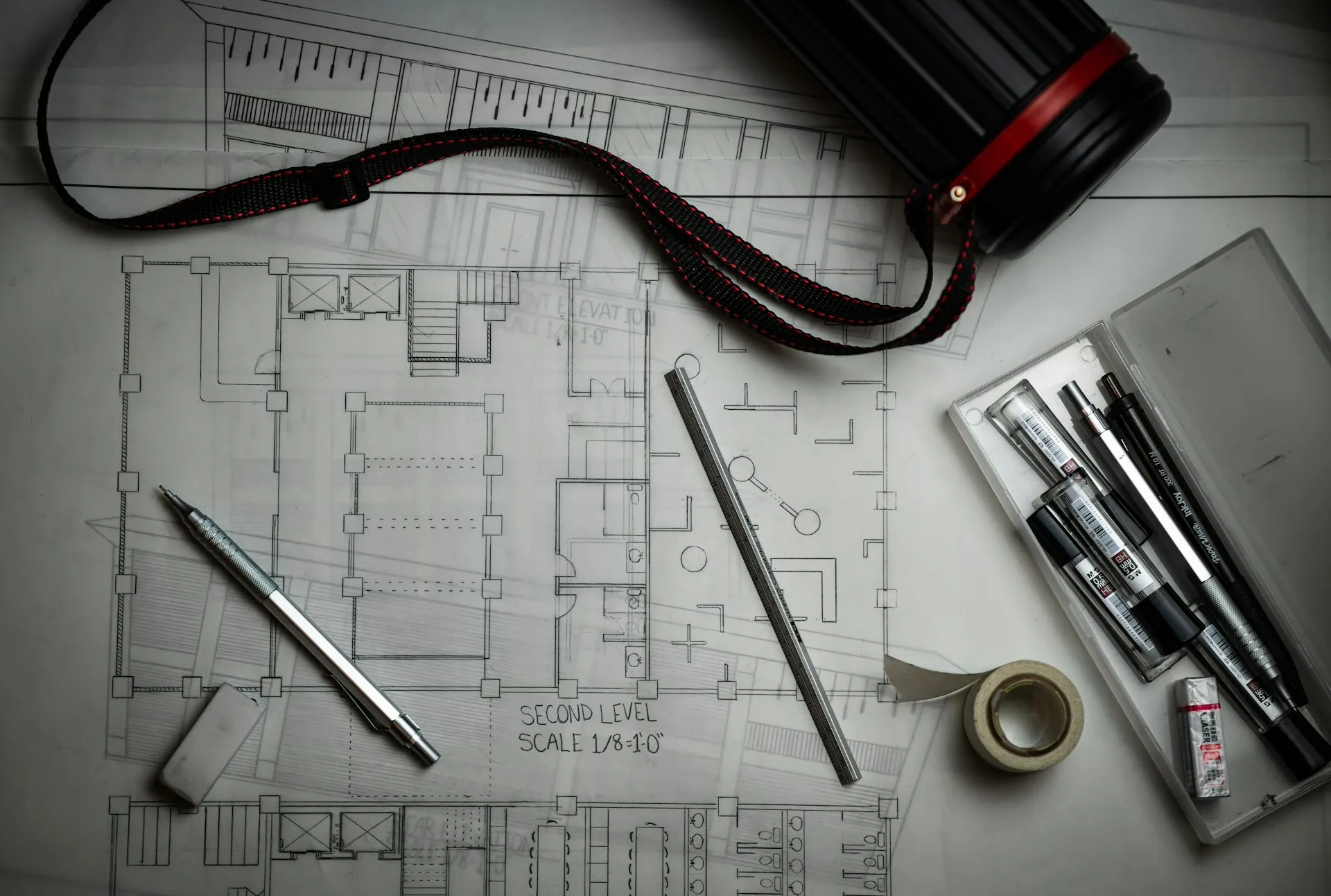 Building drawings on a desk with drafting pencils, a metal ruler and a drawing tube